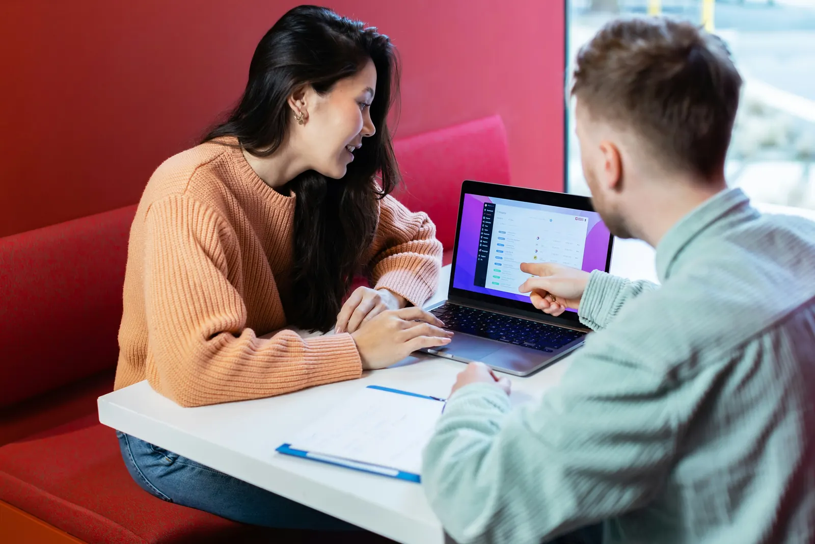Twee mensen bekijken samen een laptop en documenten aan een tafel op kantoor